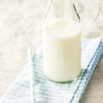 A glass of milk on the table with a spoon.