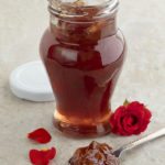 A jar of tea next to a muffin and rose petals.